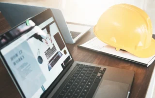 A laptop showcasing construction company website marketing next to safety equipment and paperwork