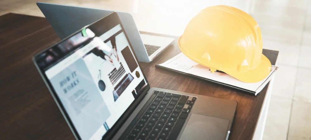 A laptop showcasing construction company website marketing next to safety equipment and paperwork