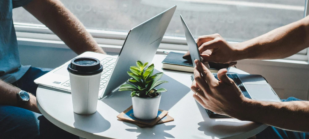 Two individuals meeting with open laptops and coffee, reviewing digital marketing strategies and B2B marketing partners