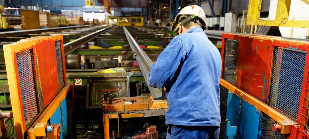 Manufacturing company marketing worker inspecting metal rail in industrial factory setting.